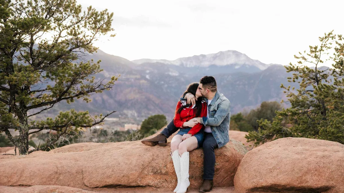 Couple embracing on warm red sandstone with mountain ridges behind them during a Sedona Arizona photoshoot session