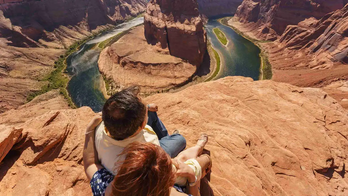 Couple seated at the rim of Horseshoe Bend above the looping Colorado River during an Arizona photoshoot